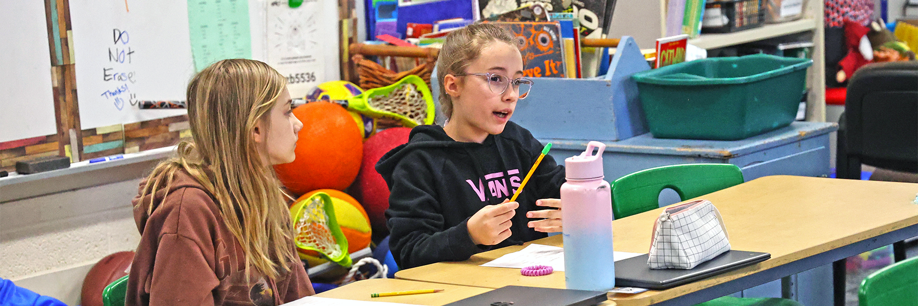 Two girls at desk one asking question