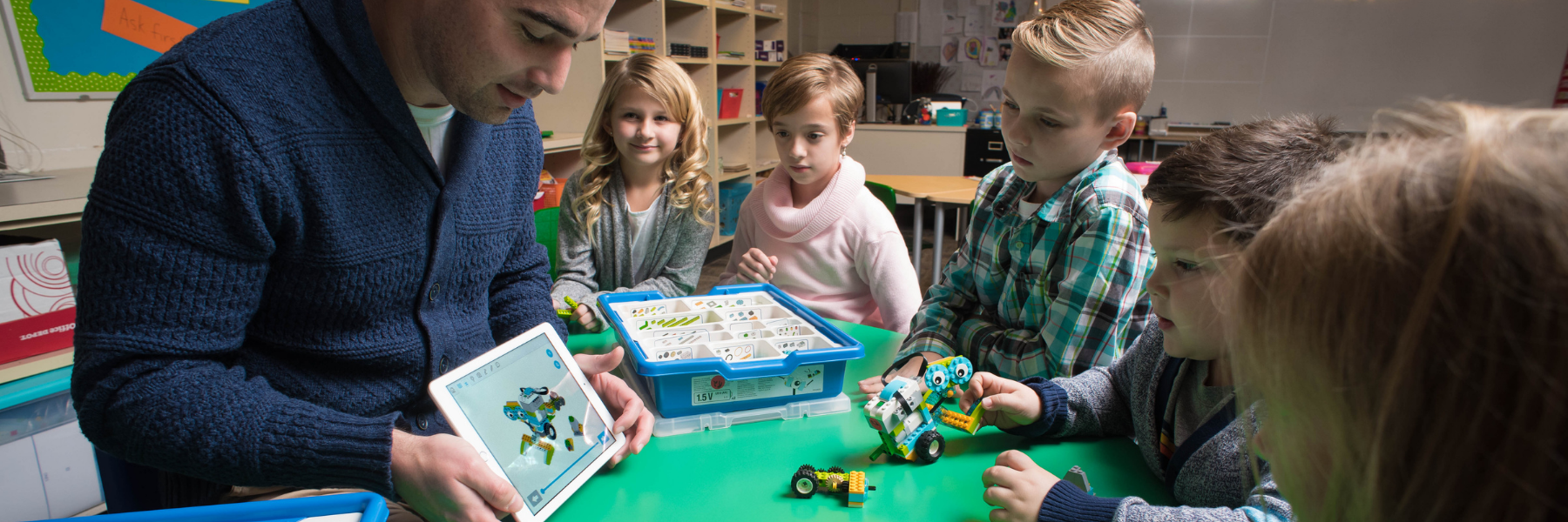 A teacher and students work through a coding problem using robotics materials and an iPad.