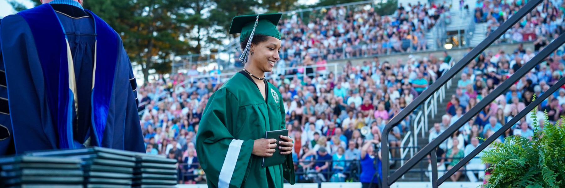 A female student walks across the stage at commencement with the audience in the background.